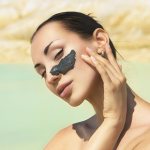 Девушка у моря с мазком чёрной глины на лице